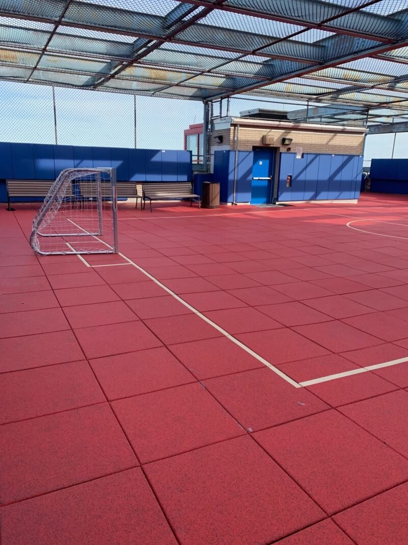 Rooftop playground with red safety tiles, soccer goal and protective netting